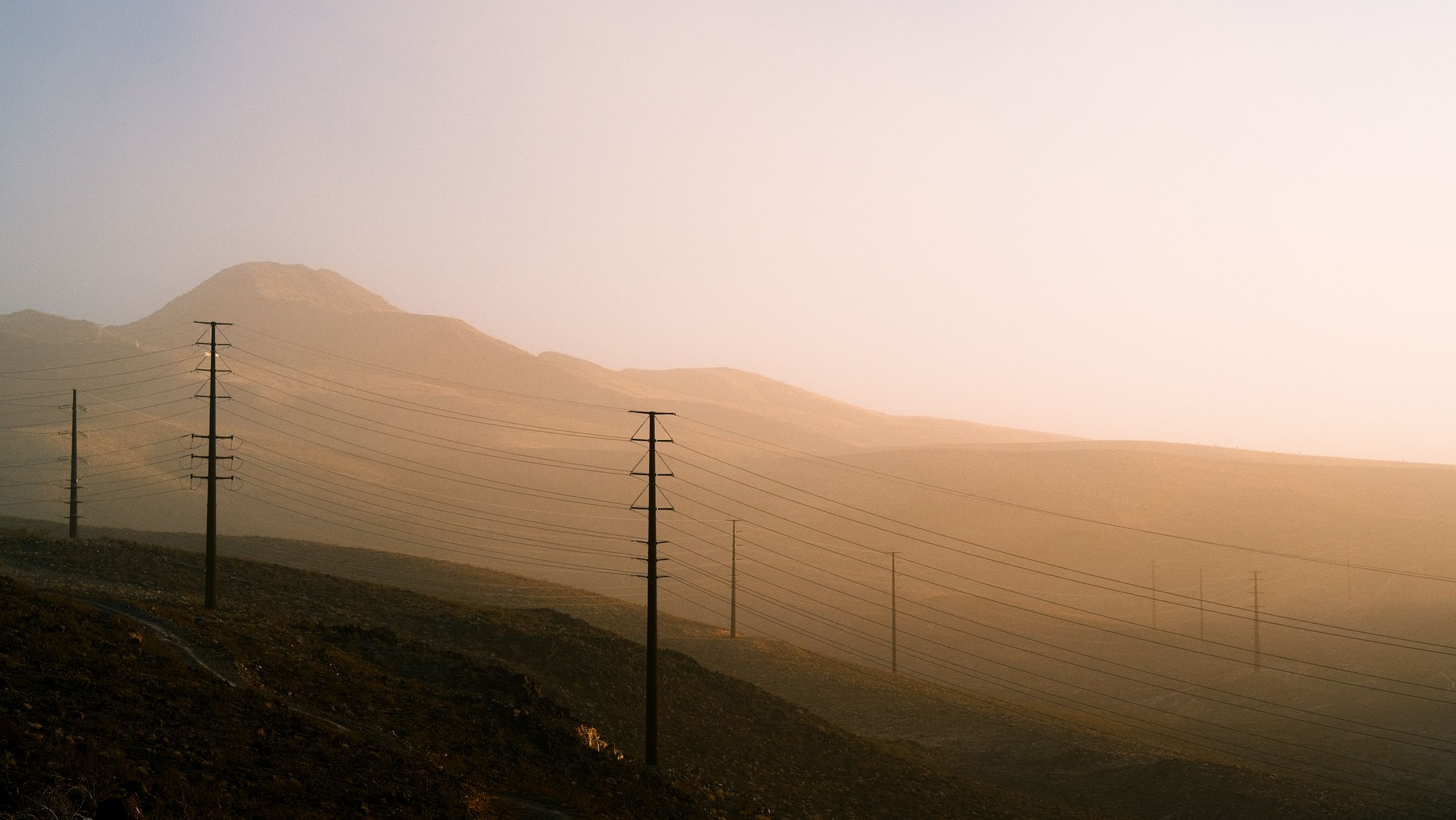 Power lines crossing desert hills in golden haze